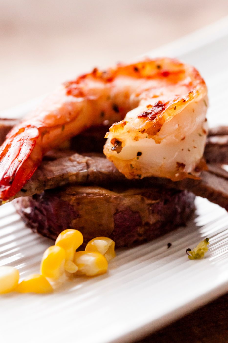 Grilled shrimp on a sliced steak with sweet corn, served on a white plate